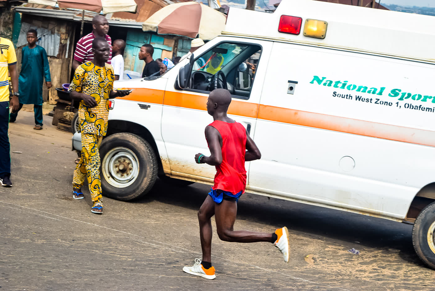 A runner in a red vest passing spectators on a street